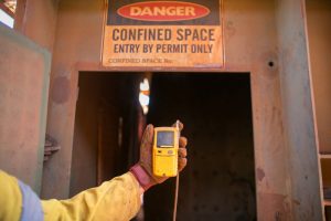 Constructor worker hand holding gas test leak detector device while commencing safety gas testing atmosphere at main entry and exit on confined space door prior to work construction site, Australia
