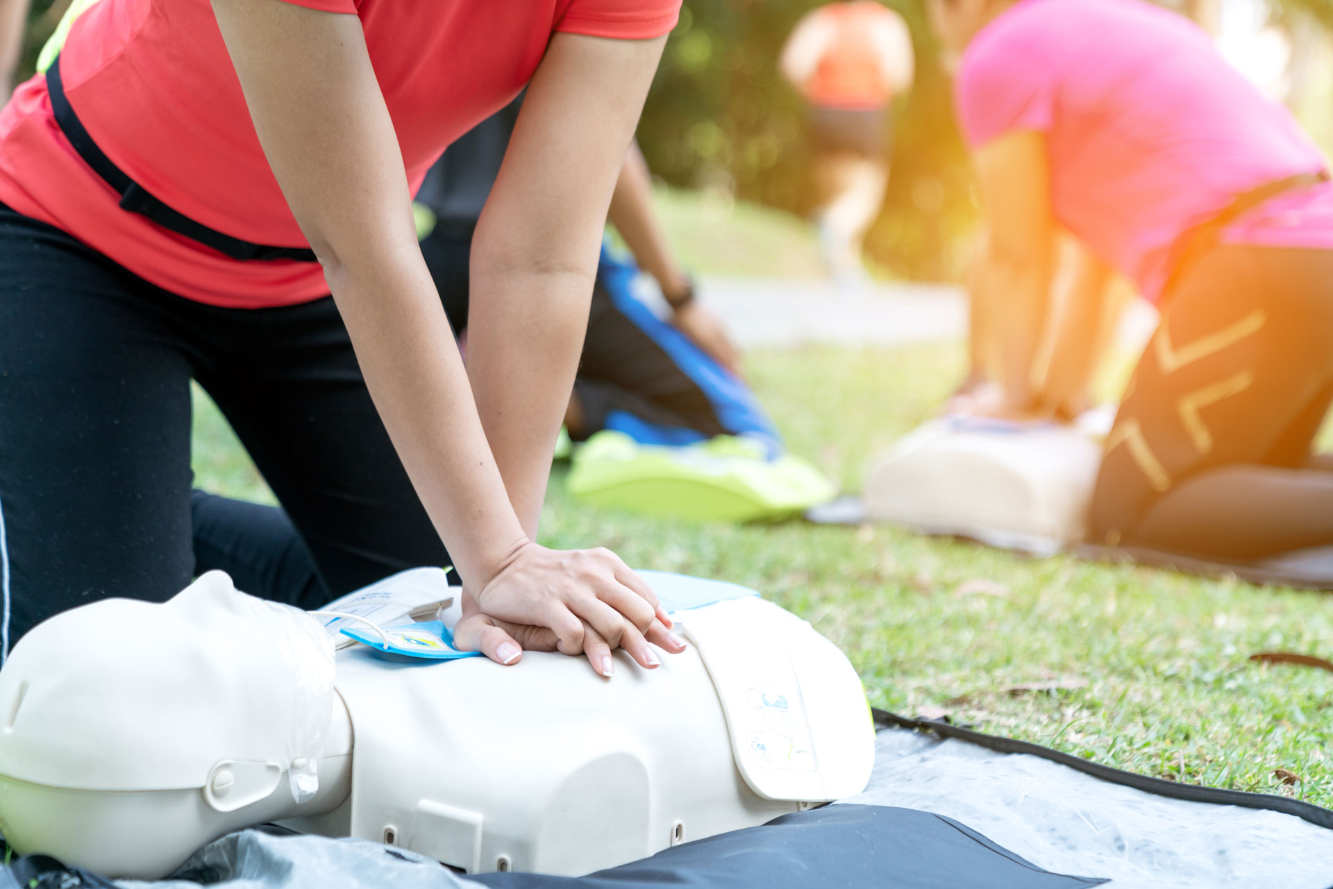 Female or runner woman training CPR demonstrating class in park by put hands and interlock finger over CPR doll give chest compression